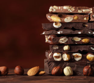 Light and dark chocolate bars with nuts layered on a brown background