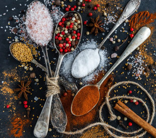 Commonly fraudulent herbs and spices sit in spoons on a black table